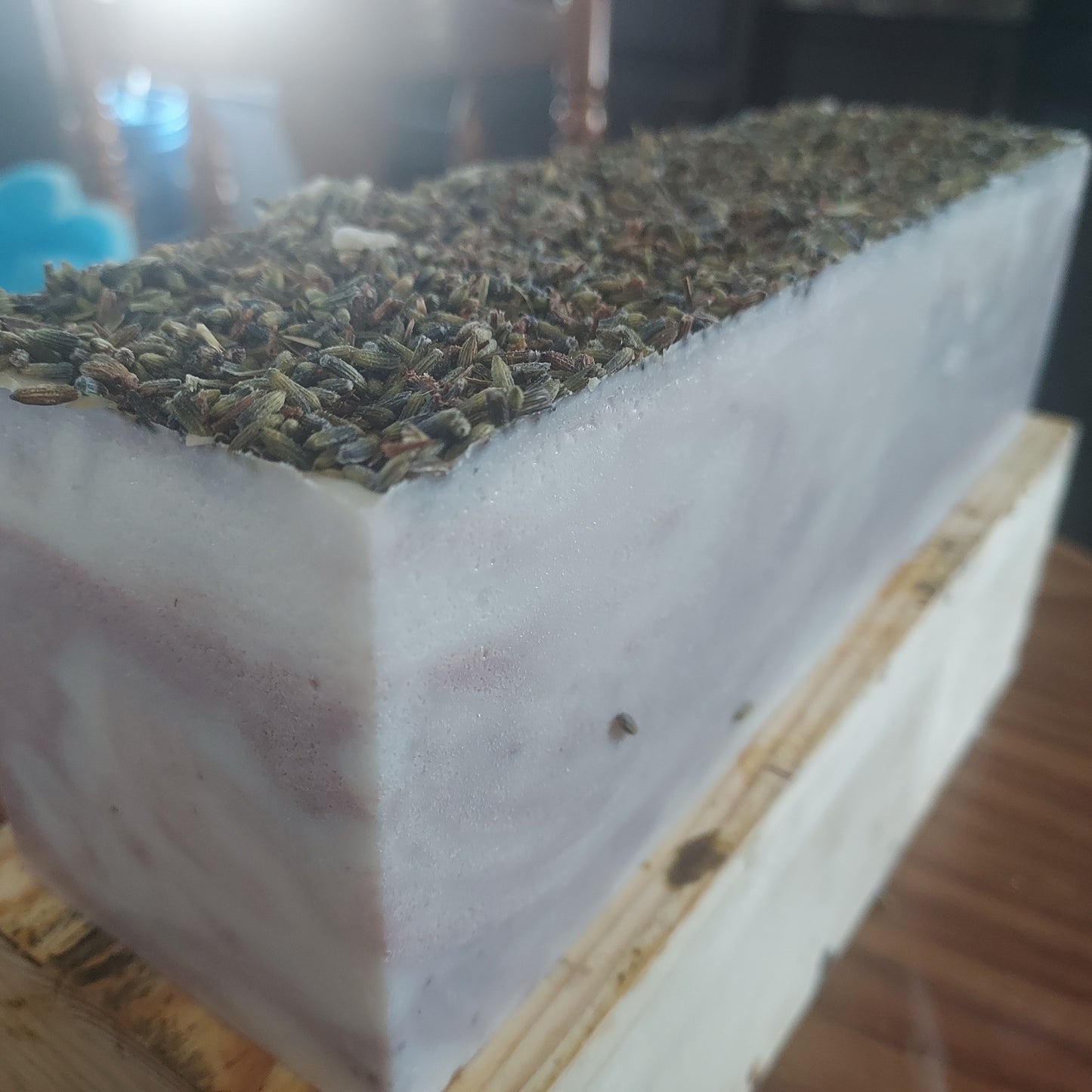 Block of Lavender soap material with lavender buds on top on a soap cutter, wooden surface