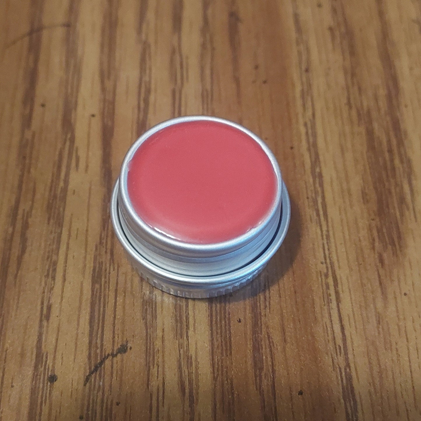 Pink lip balm inside a tin on a wooden surface
