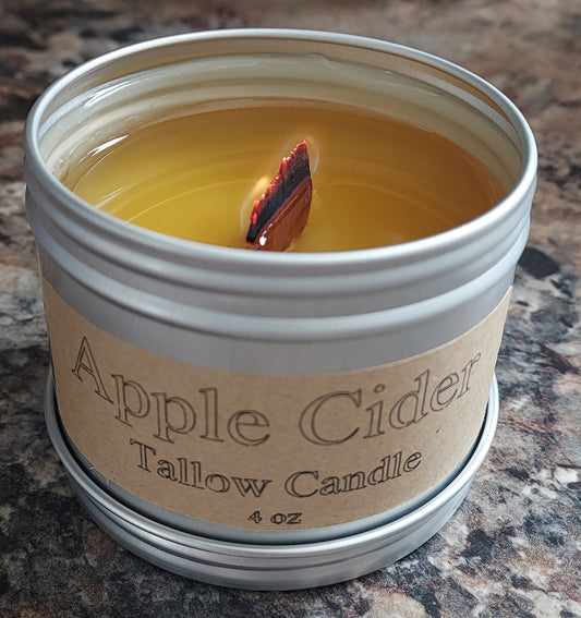 Candle in a tin labeled 'Apple Cider Tallow Candles' on a marble surface.