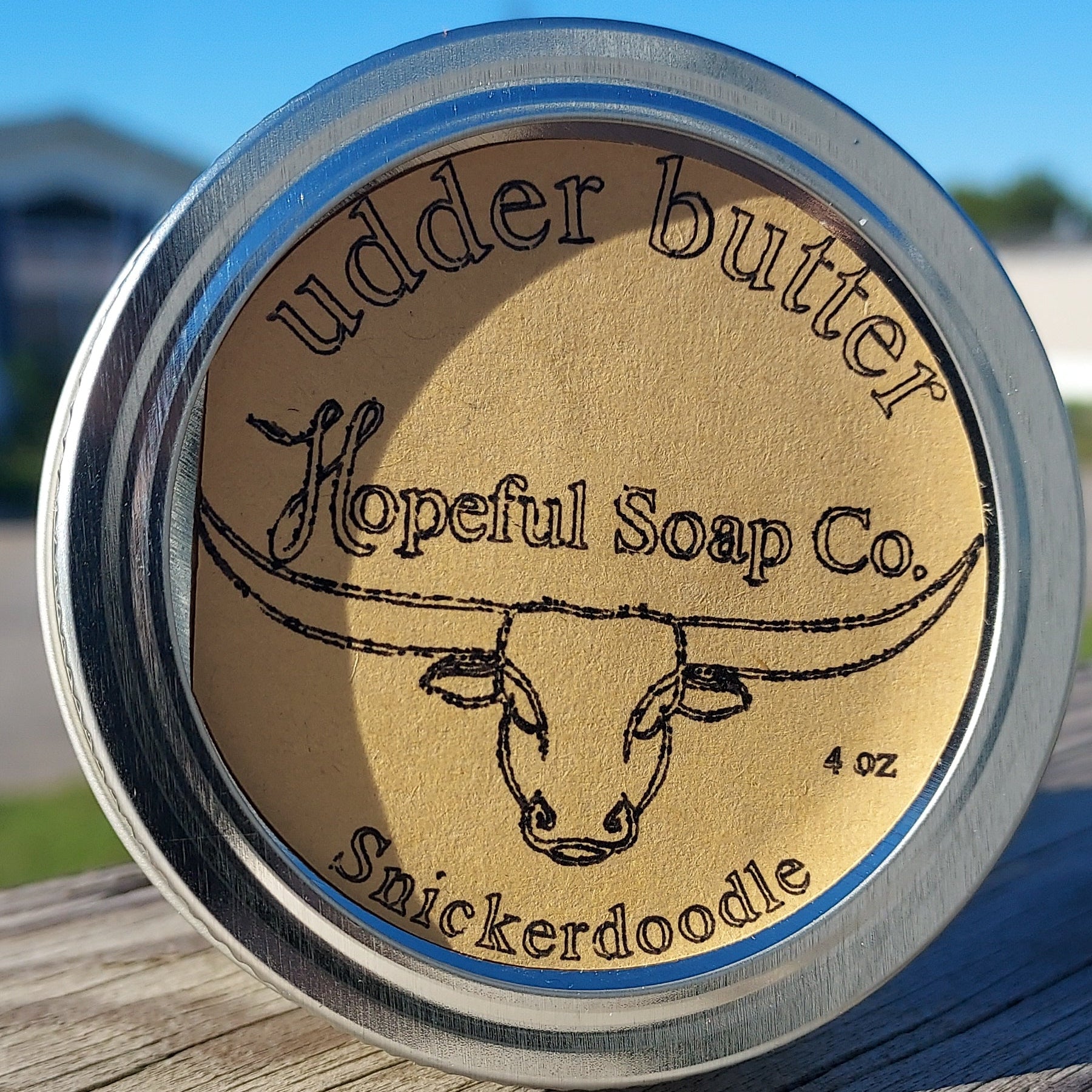 Metallic container with wooden lid featuring branding on a wooden surface.